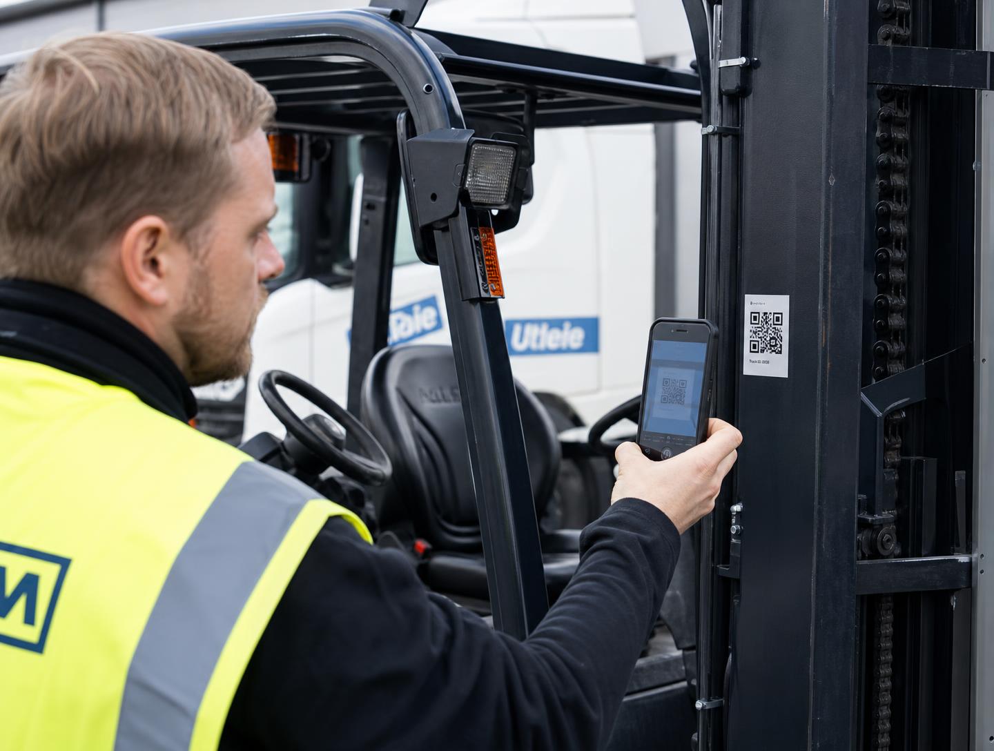 Ansatt i vernevest skanner QR-koden på siden av en gaffeltruck med mobilen